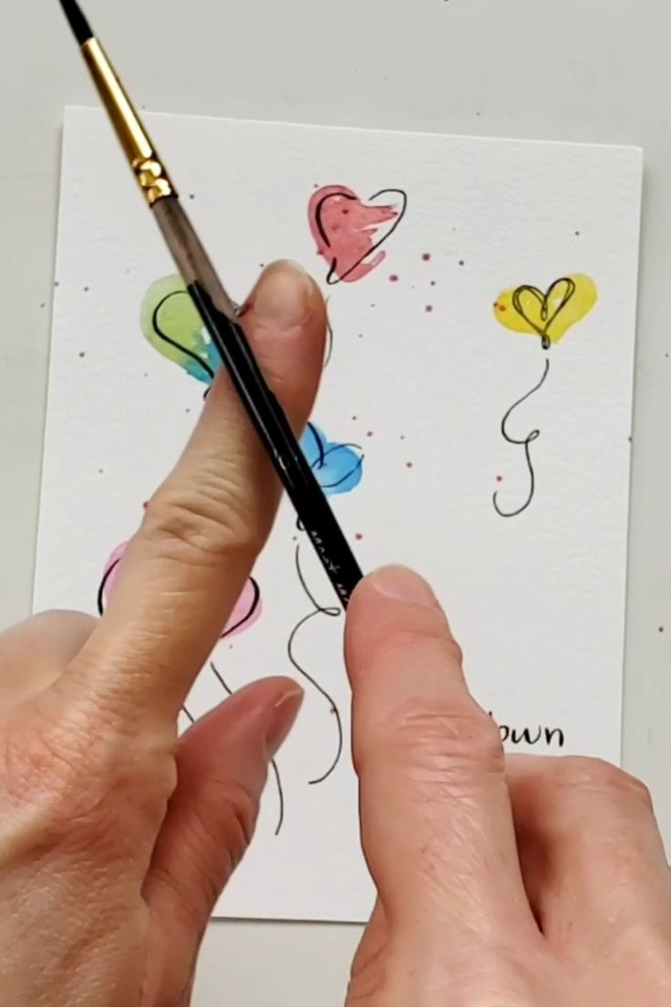 a person is holding a pen and drawing hearts on a piece of paper with colored pencils