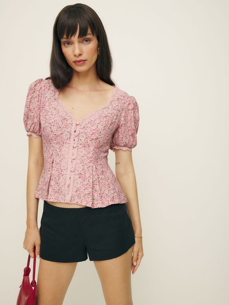 Up top. Shop the Minette Top from Reformation, a fitted top with a v-neckline, button front, short puffed sleeves, and lace detailing. Feminine Fitted V-neck Puff Sleeve Top, Feminine V-neck Tops With Button Closure, Feminine V-neck Top With Button Closure, Feminine Fitted V-neck Blouse, Fitted V-neck Puff Sleeve Top, Spring Fitted V-neck Puff Sleeve Top, Fitted V-neck Puff Sleeve Top For Spring, Feminine V-neck Fitted Puff Sleeve Top, Fitted Feminine Puff Sleeve V-neck Top