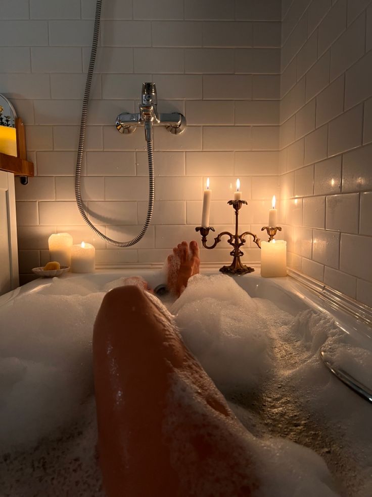 a person laying down in a bathtub with candles on the side and one foot up