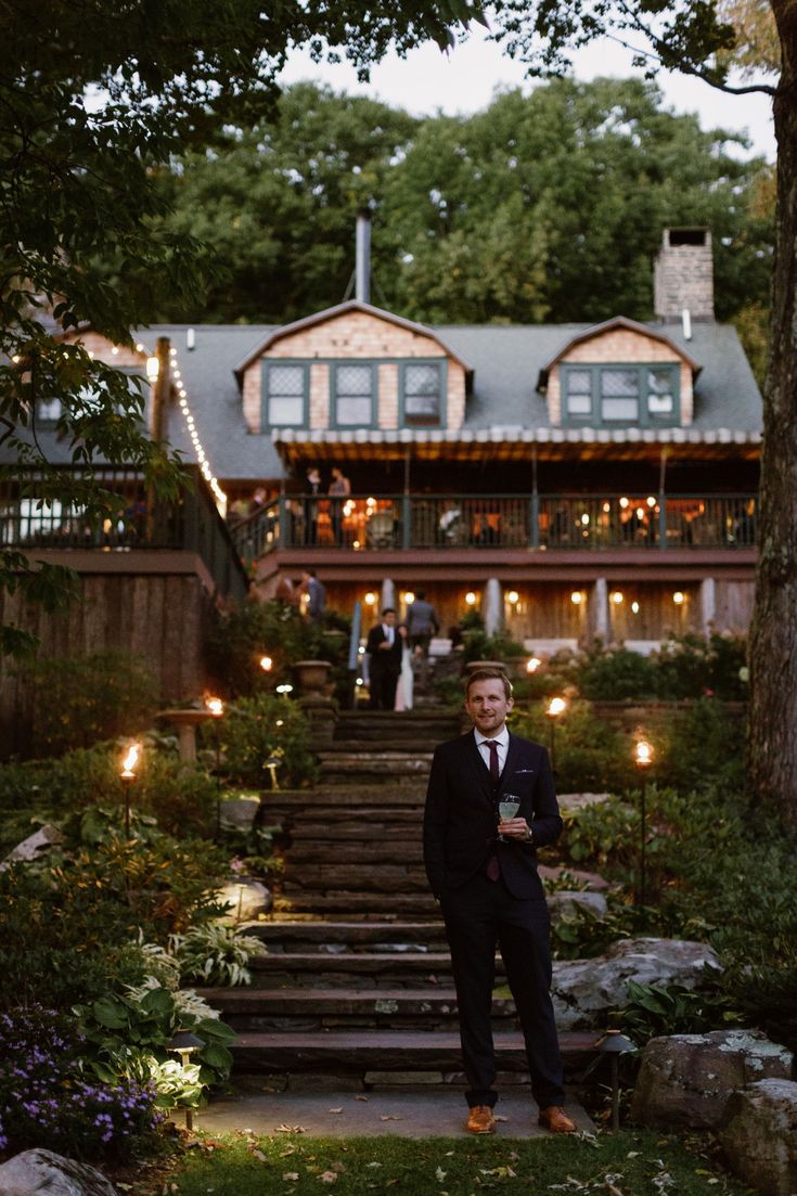 a man standing in front of a house with lights on the porch and steps leading up to it