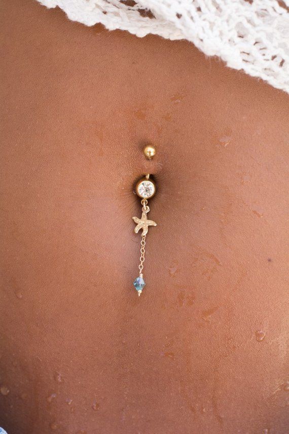 the back of a woman's stomach with a gold chain and dangling belly ring