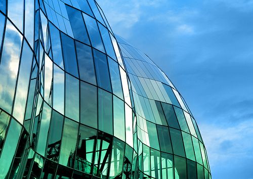 the side of a glass building with blue skies in the backgrounnd and clouds in the background