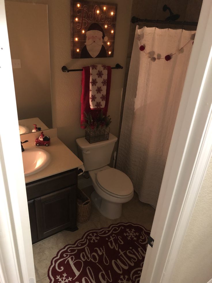 a bathroom decorated for christmas with lights on the shower curtain and santa clause sign above the toilet