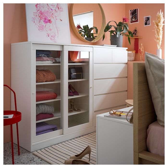 a white cabinet with drawers and shelves filled with folded clothes next to a red chair