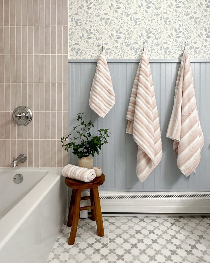 three towels hanging on the wall next to a bathtub and stool with a potted plant