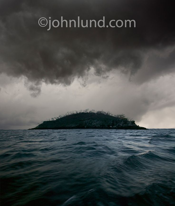 an island in the middle of the ocean under a dark sky with storm clouds above it