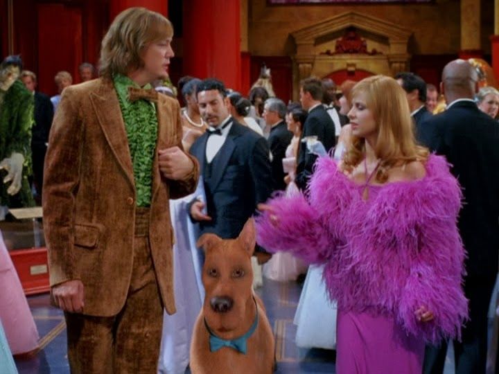 a man in a tuxedo standing next to a woman with a dog on her lap