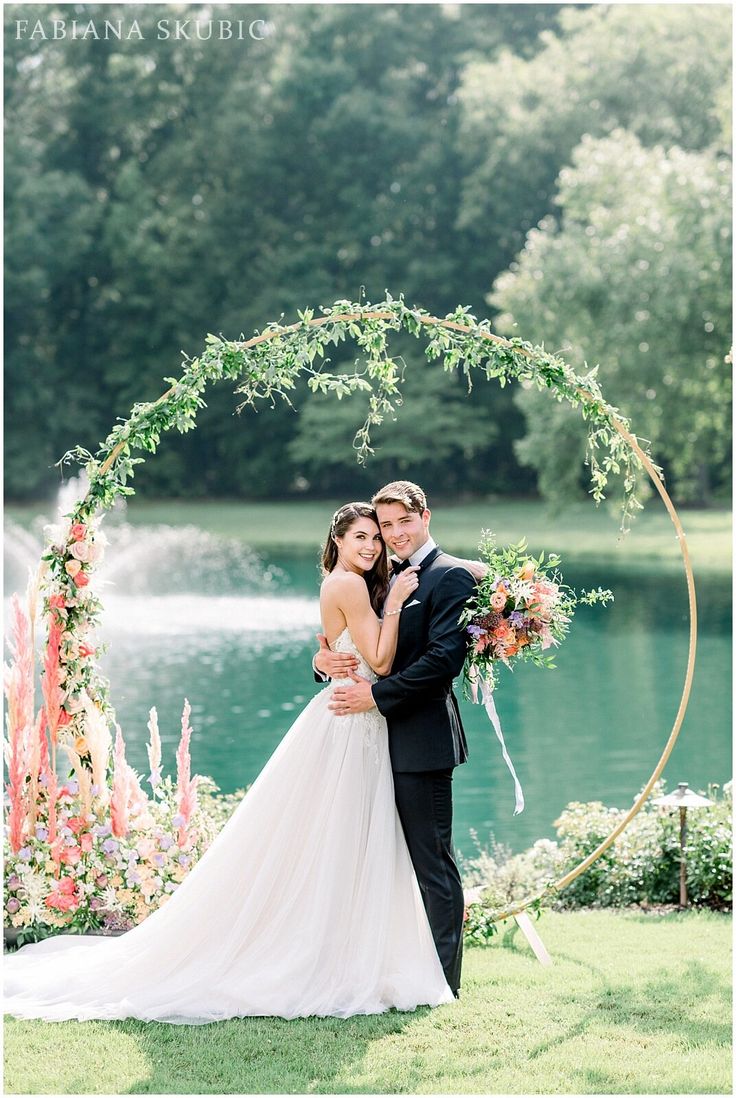 a bride and groom pose for a photo in front of a floral arch at their wedding