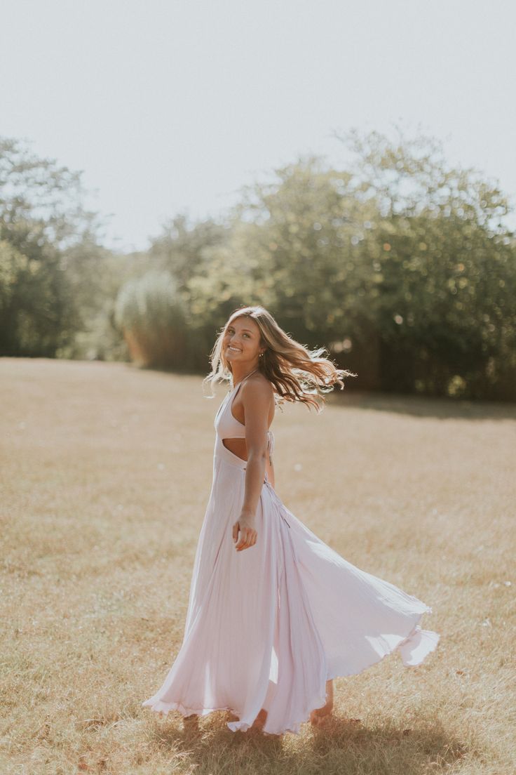 a woman in a white dress is walking through the grass with her hair blowing in the wind