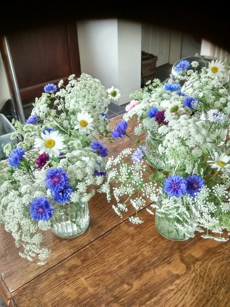 three glass vases filled with flowers on top of a wooden table in front of a mirror