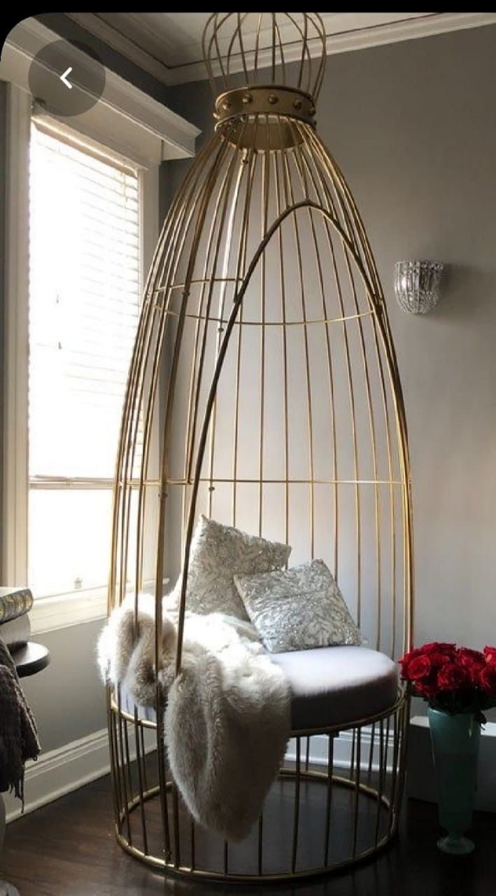 a gold birdcage with white pillows and fur on it in a living room