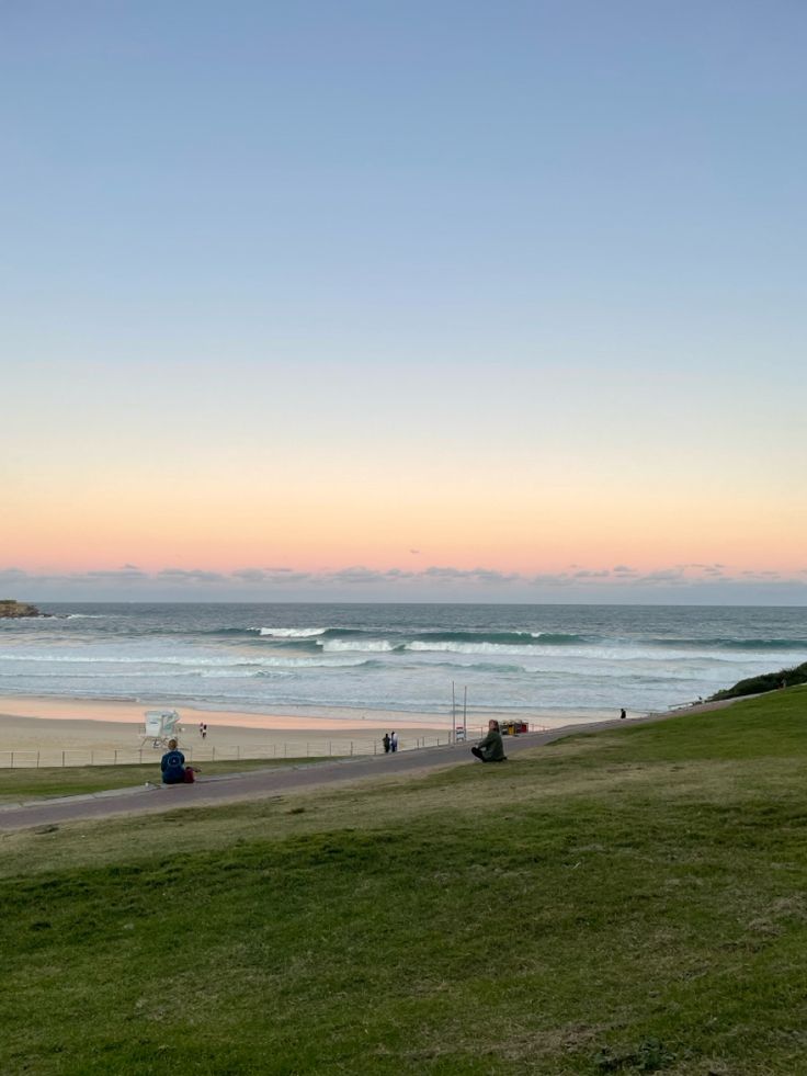 people are walking along the beach at sunset