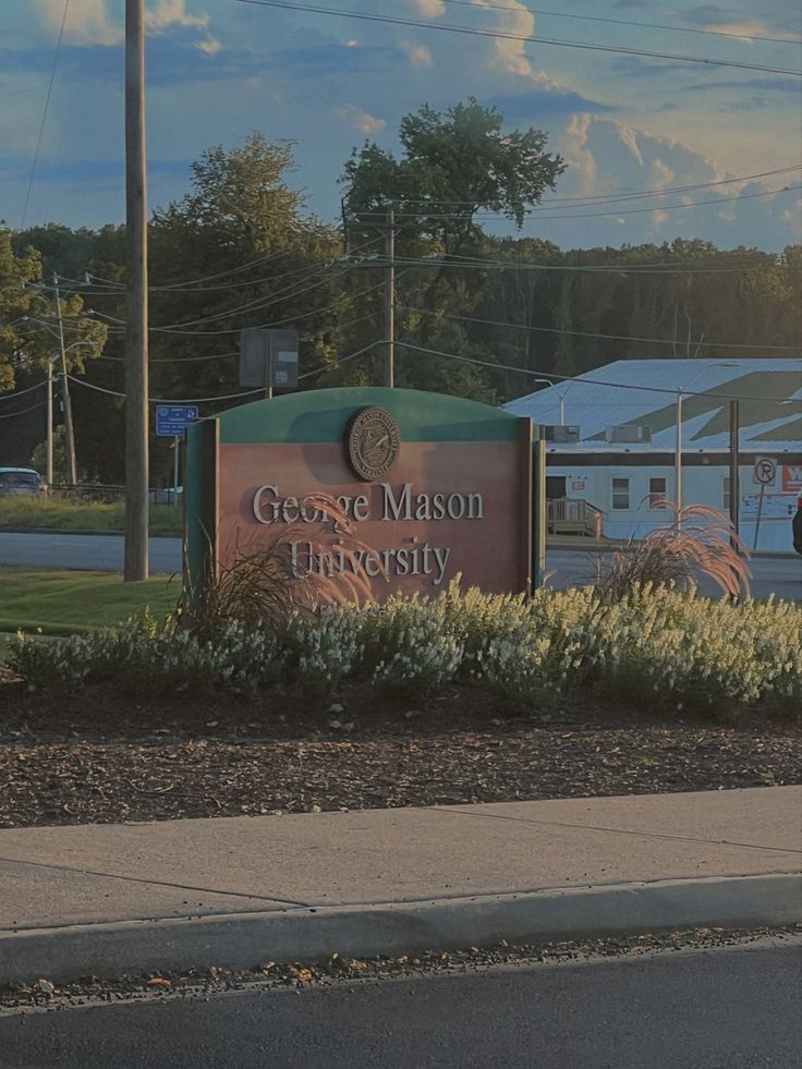 a sign for george mason university in front of some bushes and trees on the side of the road