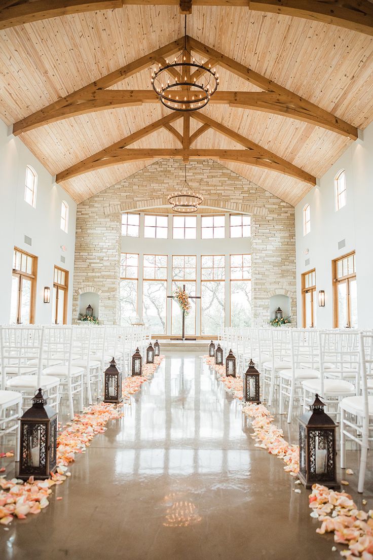 the aisle is lined with white chairs and rose petals on the floor, along with lanterns