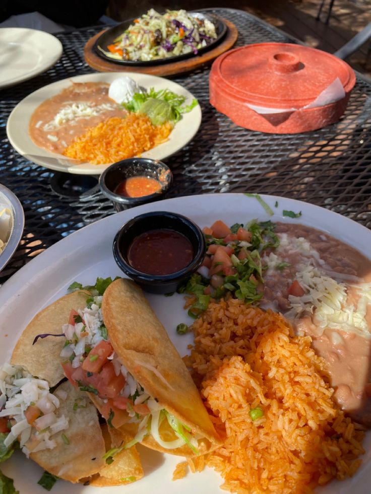 mexican food is served on a plate at an outdoor table with condiments and sauces