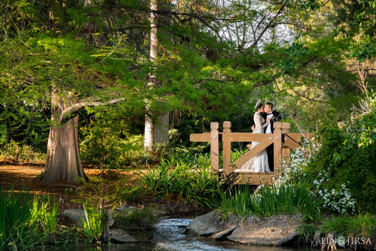 a bride and groom standing on a bridge over a stream