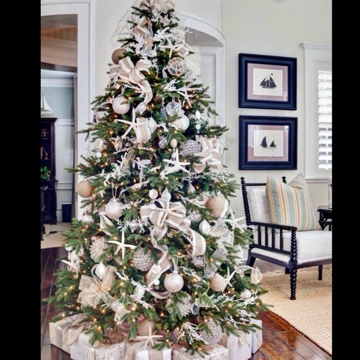 a decorated christmas tree in a living room with white and silver ornaments on the top