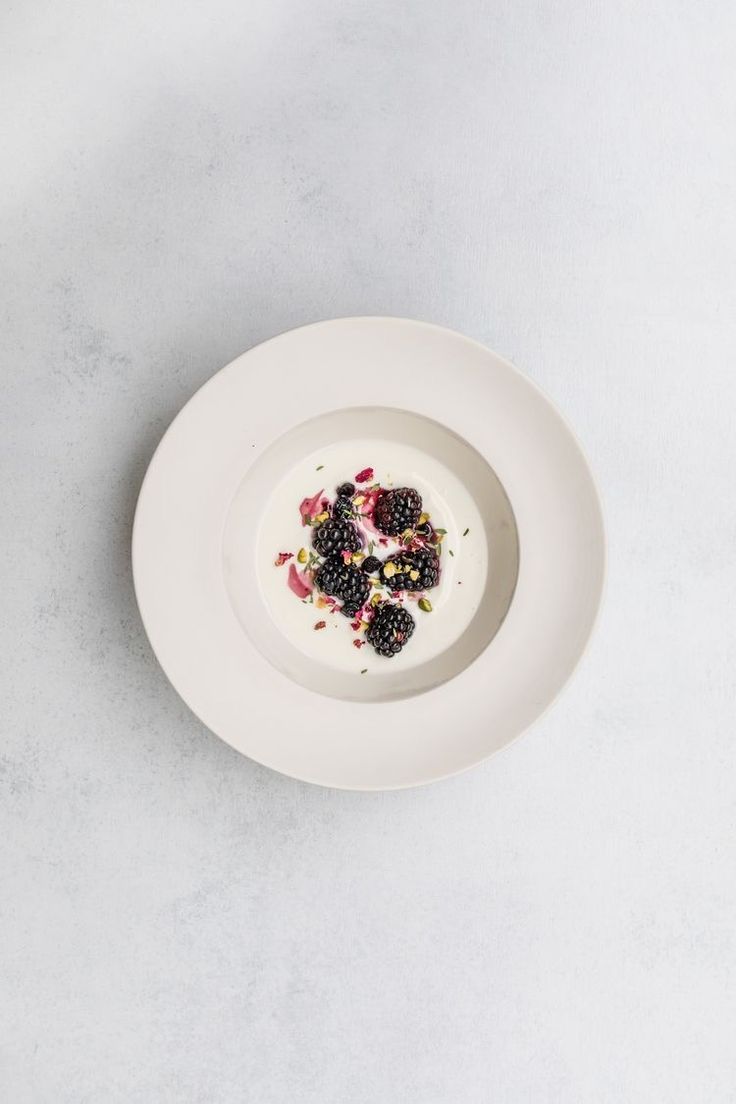 a white plate topped with fruit and yogurt on top of a marble table