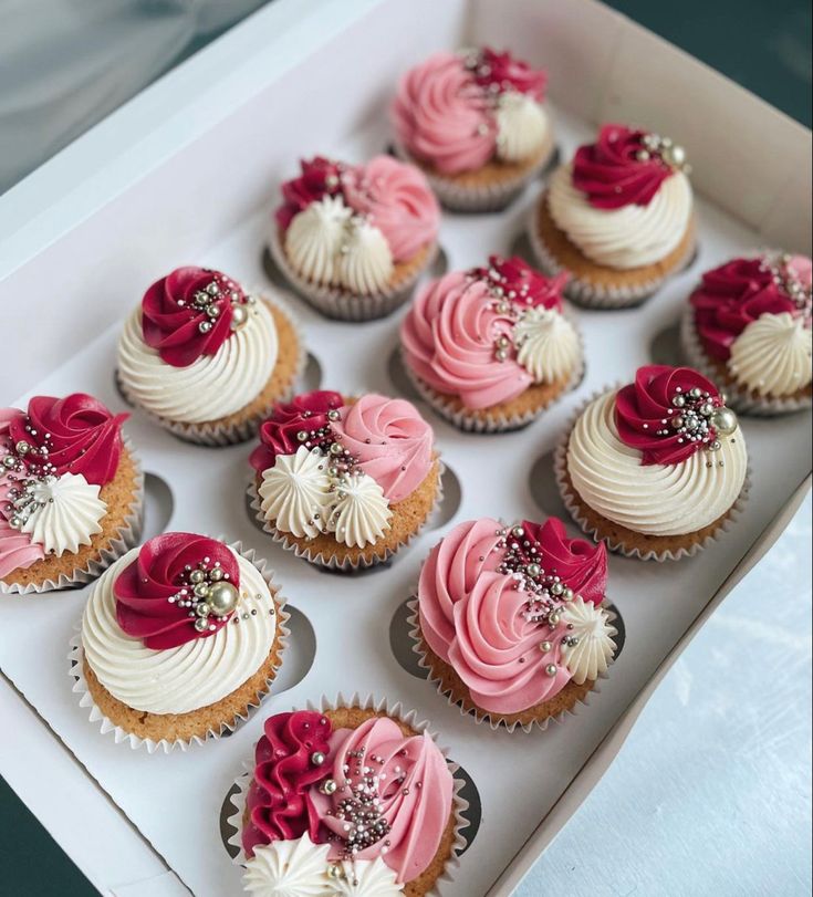 twelve cupcakes with pink and white frosting in a box