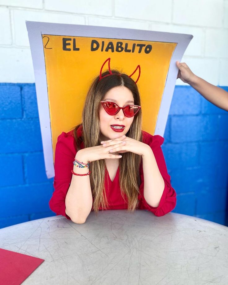 a woman in red shirt and sunglasses sitting at table with devil sign above her head