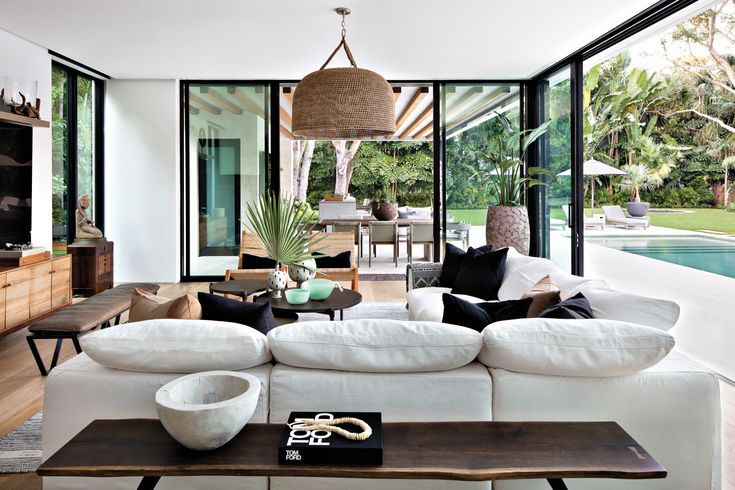 a living room filled with white furniture and lots of glass doors leading to an outdoor swimming pool