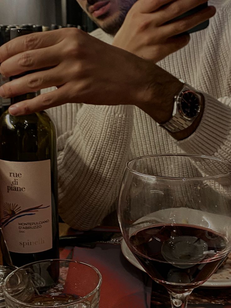 a man holding a bottle of wine in front of two empty glasses on a table