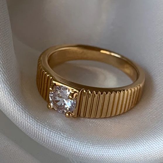 a gold ring with a white diamond on the top and bottom, sitting on a white cloth