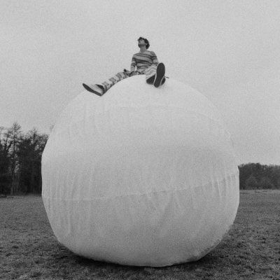 a man sitting on top of a large white ball in the middle of a field