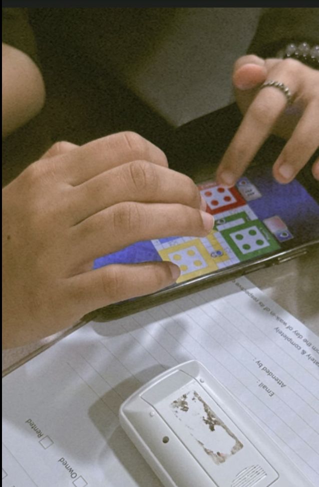 two people are playing on their cell phones at a table with papers and other items