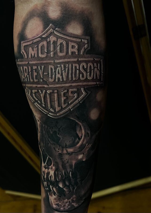 a man's arm with a skull and harley davidson logo on it, while he is holding his hand up to the camera