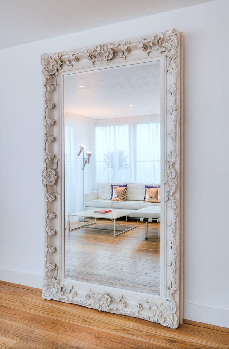 a large white mirror sitting on top of a hard wood floor next to a couch