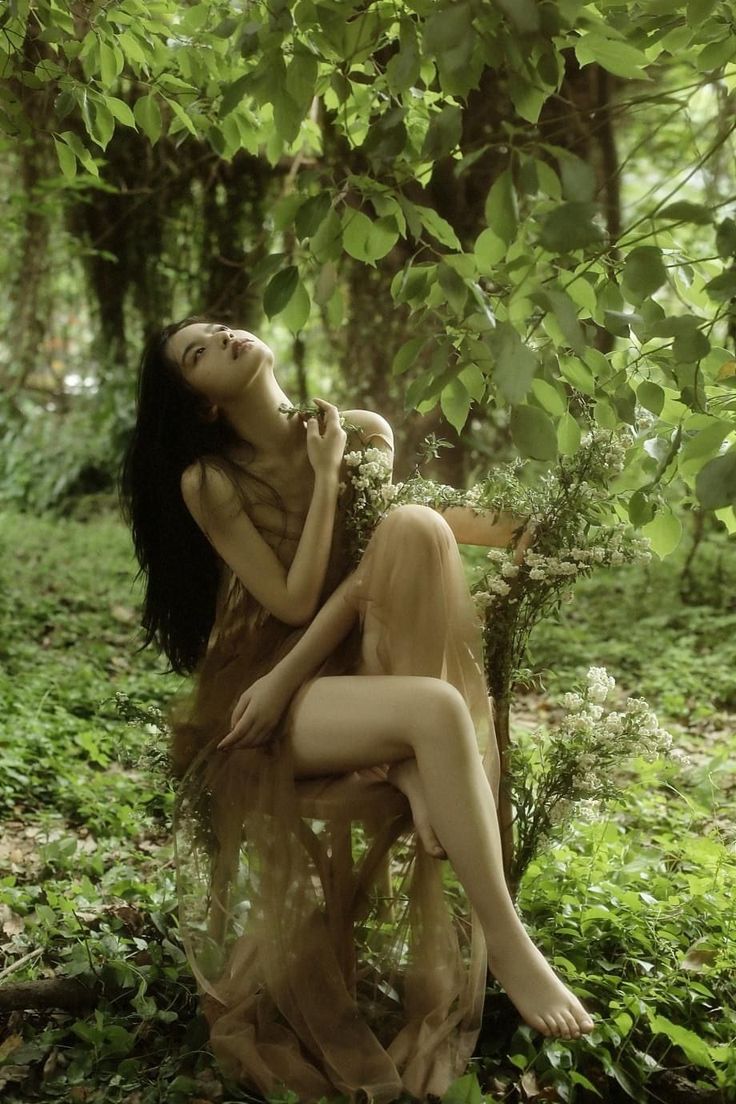 a naked woman sitting in the middle of a forest with her head on her hand