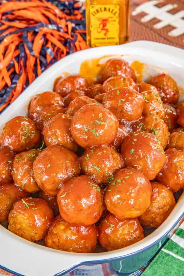 a white bowl filled with glazed meatballs next to a bottle of fireball glaze