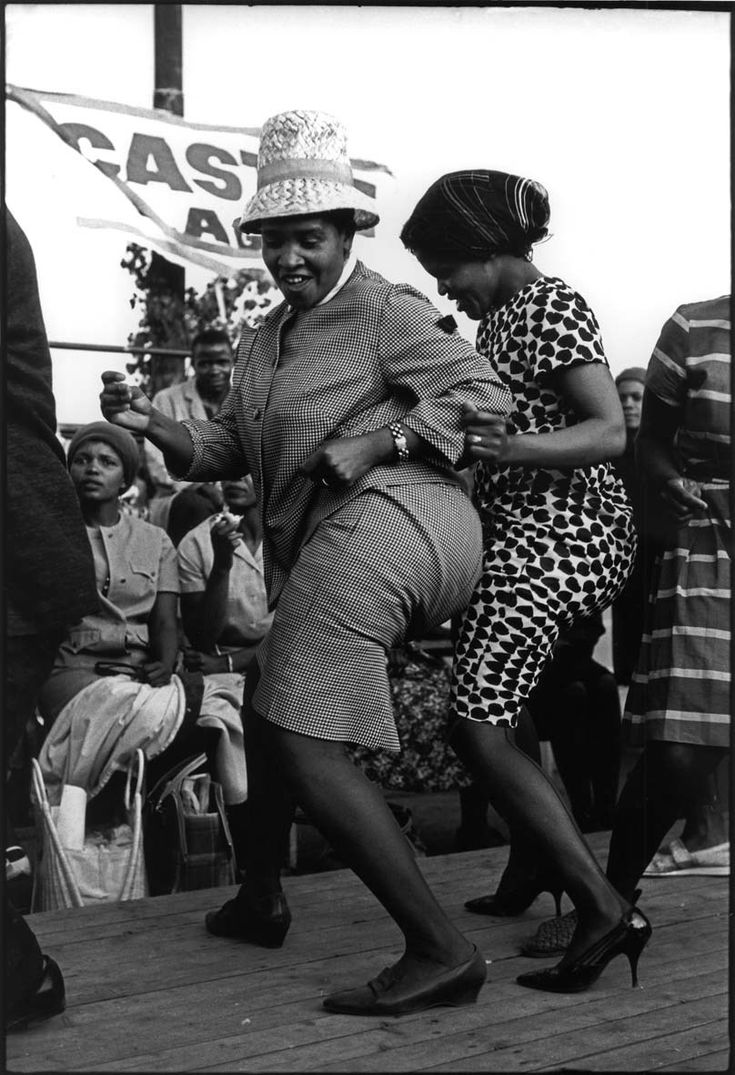 an old black and white photo of two women dancing on the boardwalk with people watching