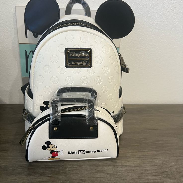 a white backpack with mickey mouse ears on it sitting next to a stack of books