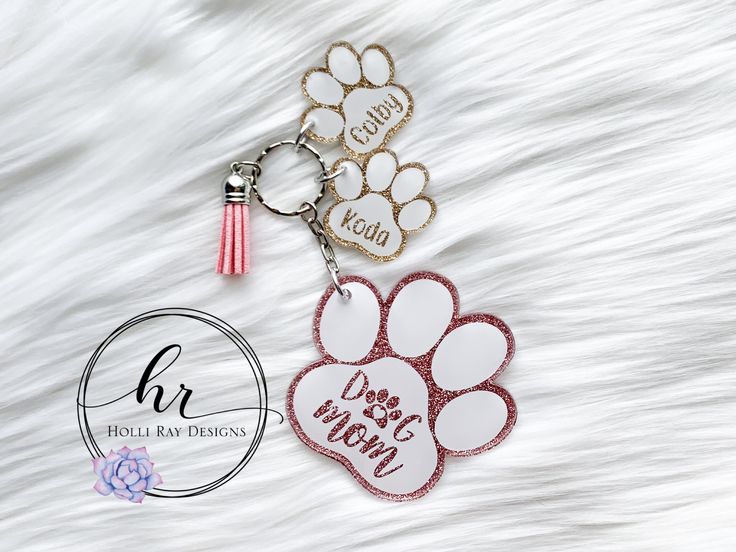 two dog paw keychains with their names on them, one is red and the other is white