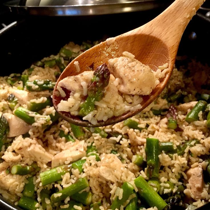 a wooden spoon filled with rice and asparagus on top of a skillet