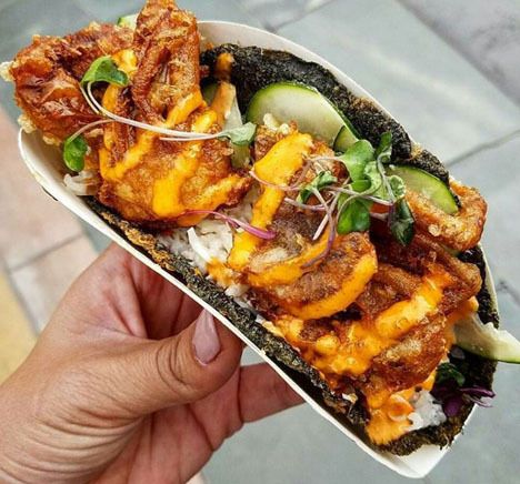 a hand holding a sandwich with meat, cheese and vegetables