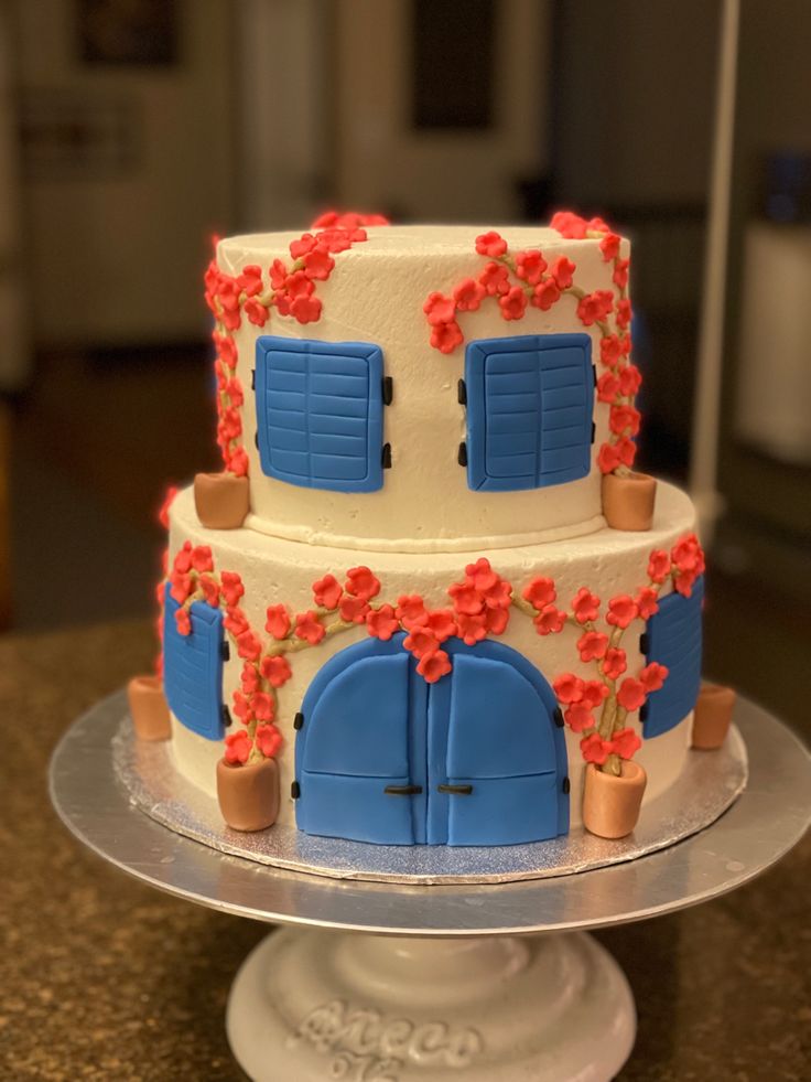 a three tiered cake with blue doors and red flowers on the top is sitting on a silver platter