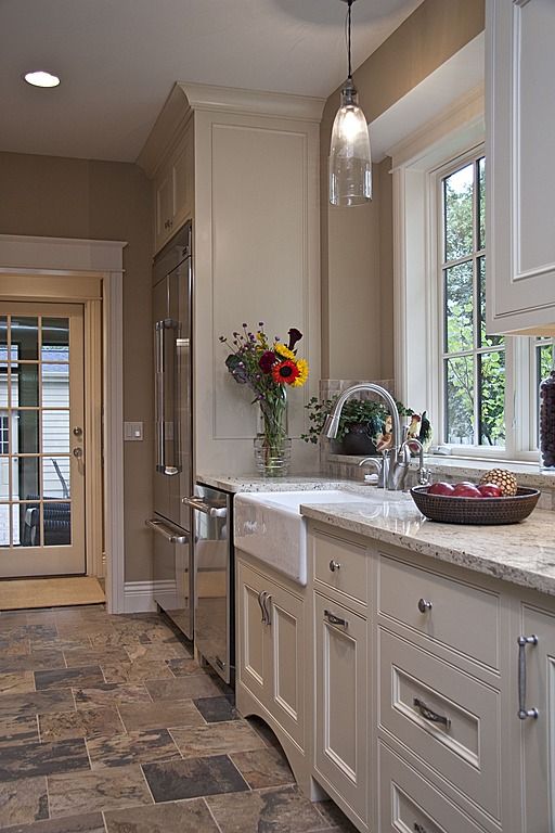 a large kitchen with marble counter tops and white cabinets, along with an open door leading to the outside