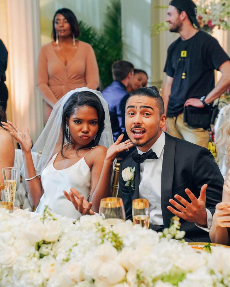 a man and woman sitting at a table with champagne glasses in front of their faces