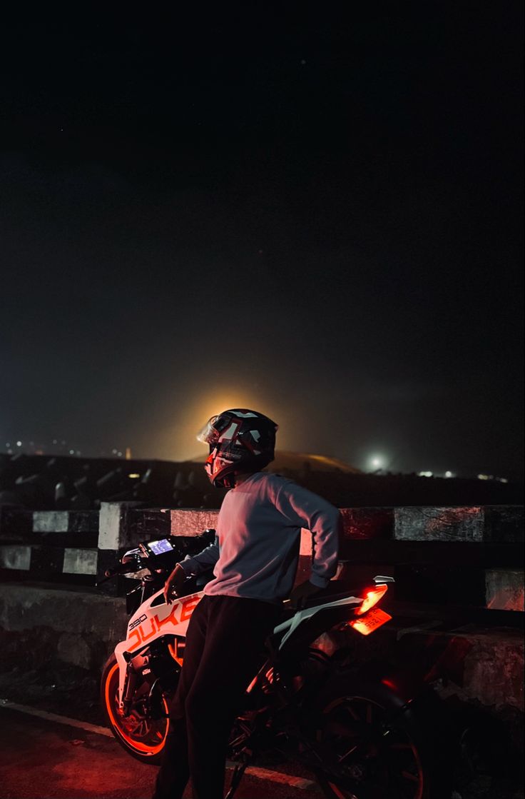 a man riding on the back of a red motorcycle at night with city lights in the background