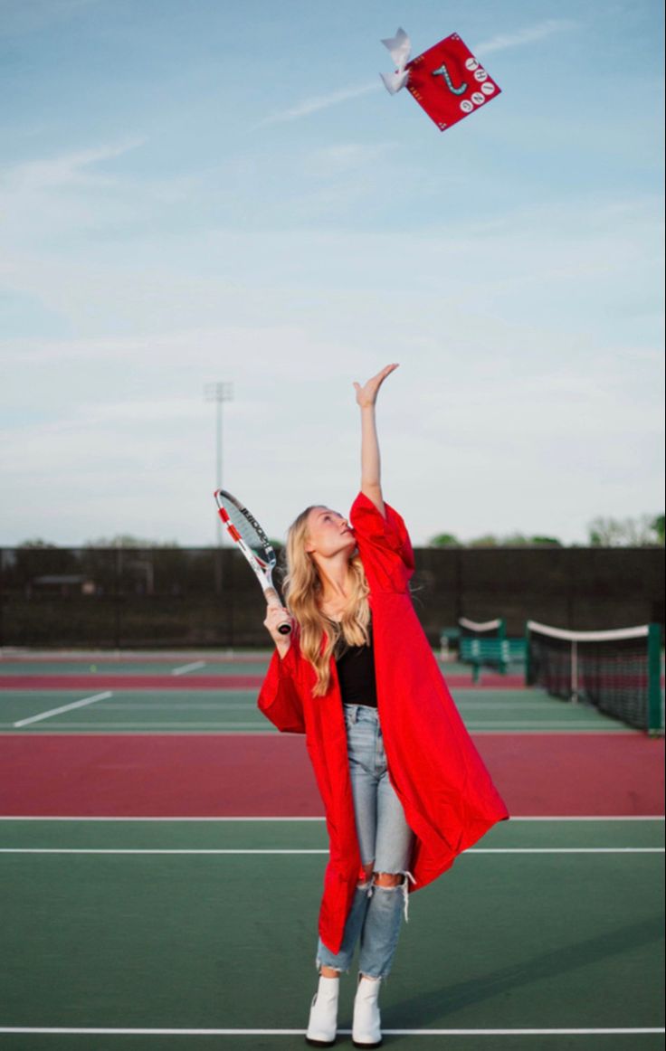 a woman in red coat flying a kite on tennis court