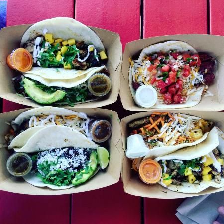 four burritos with different toppings and condiments in paper trays