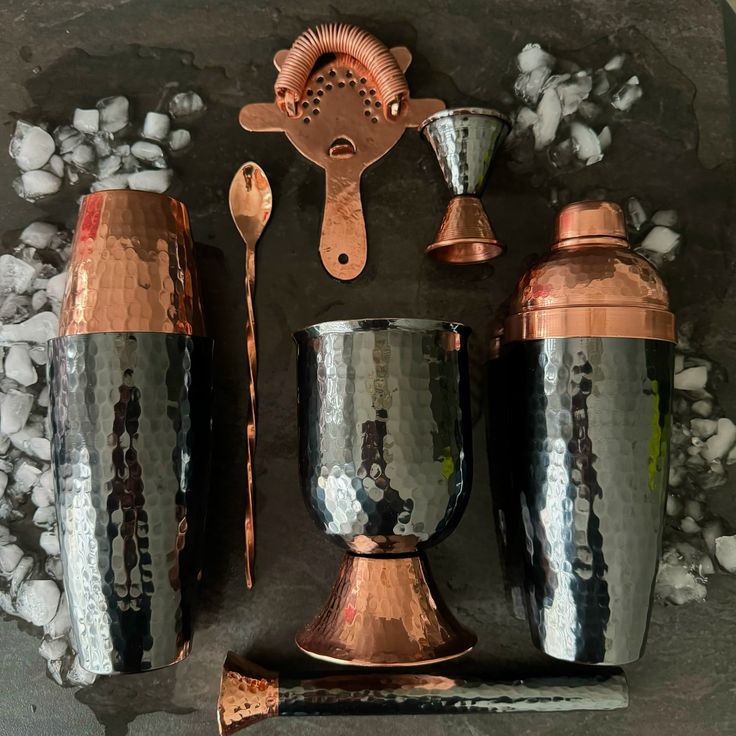 a set of copper and silver cups, spoons and utensils on top of rocks