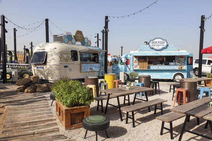 an outdoor restaurant with tables and food trucks in the background