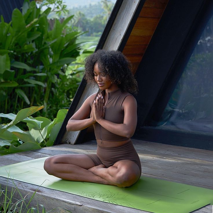 a woman in a brown dress sitting on a yoga mat and meditating with her hands together