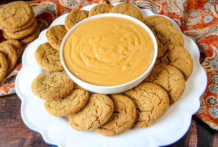 a white plate topped with cookies covered in peanut butter next to a bowl of dip