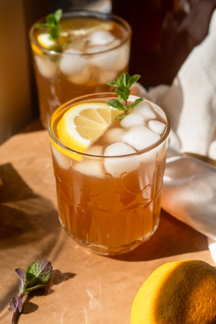 two glasses filled with ice and lemons on top of a wooden table next to an orange