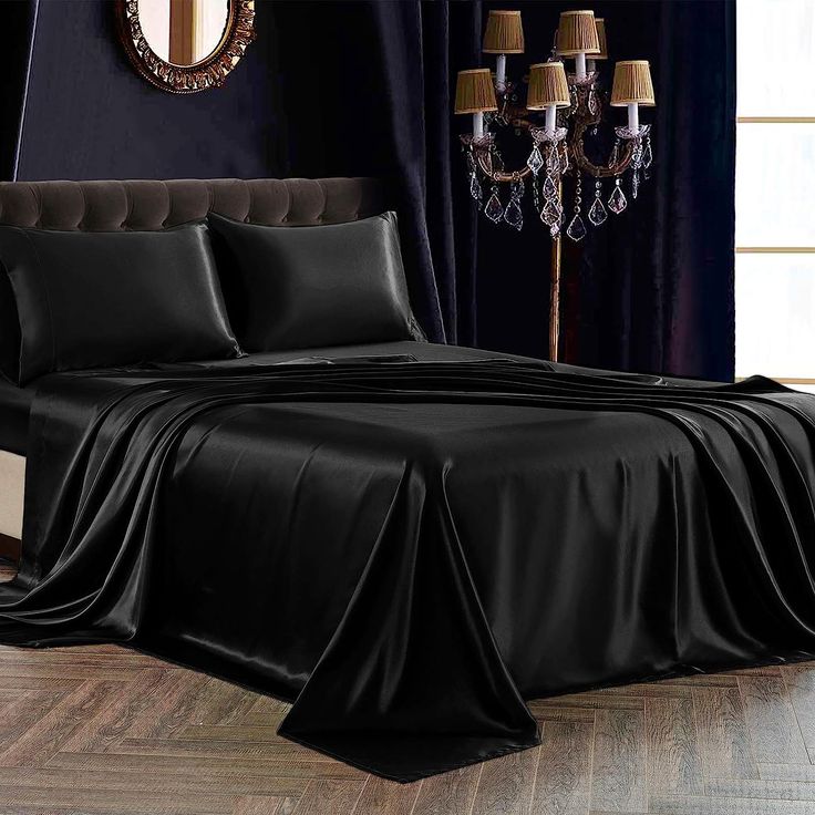 a bed with black sheets and pillows in a room next to a chandelier